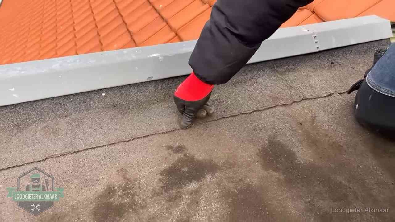 Vakman wijst een naad met vochtplekken aan op een bitumen plat dak in Alkmaar
